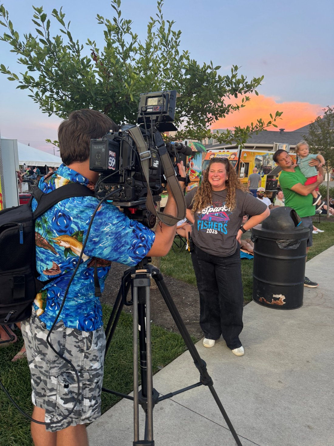 Alli Kaser in a Spark! Fishers 2025 shirt being interviewed by a Fox 59 camera operator at sunset