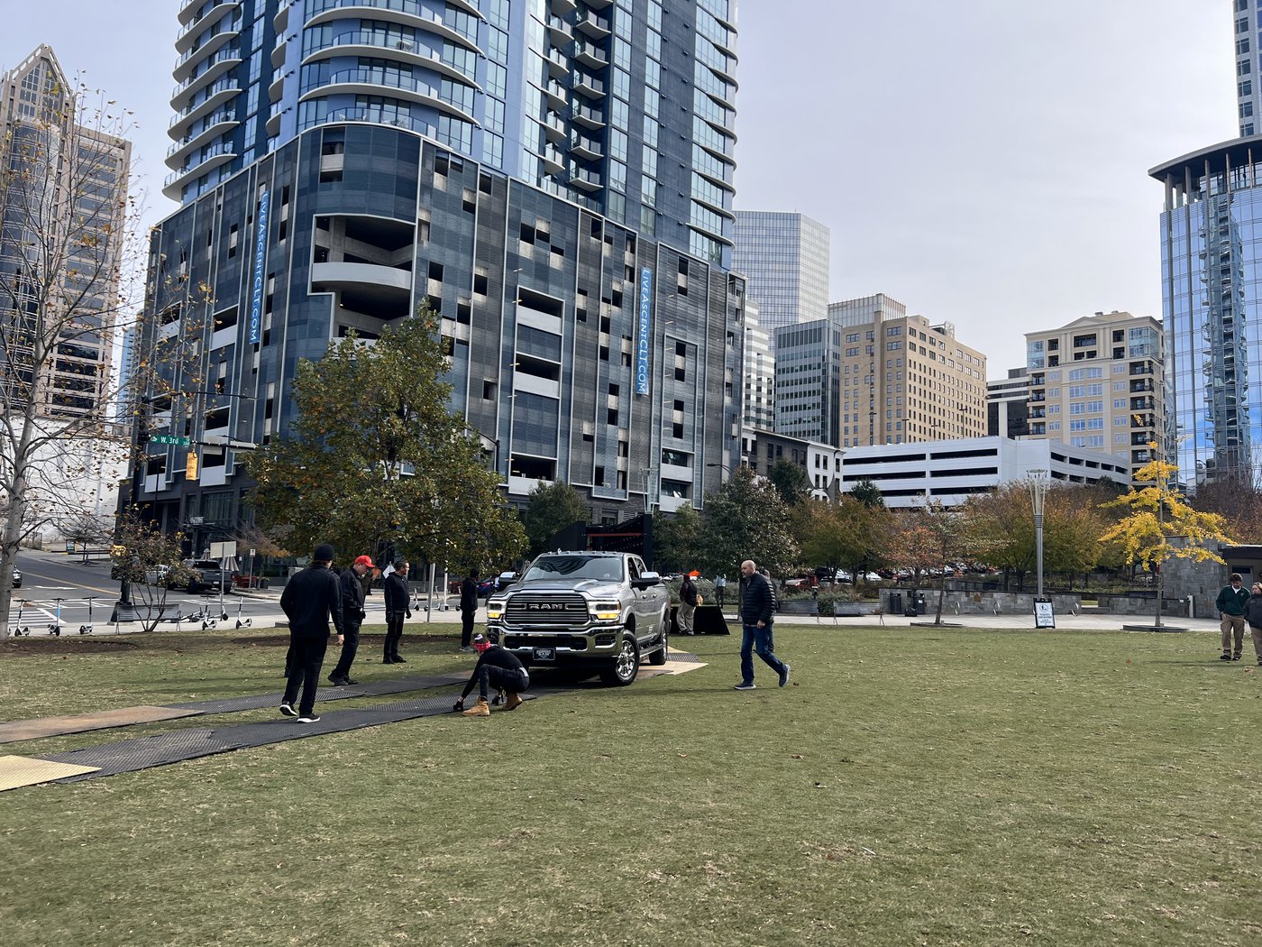 A truck being positioned on ground-protection mats on a park lawn in Uptown Charlotte while crew members look on
