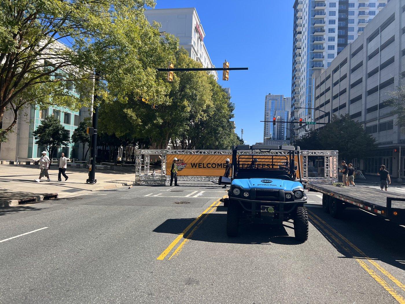 A utility vehicle and flatbed in front of a truss entrance arch on a closed street before the event opened