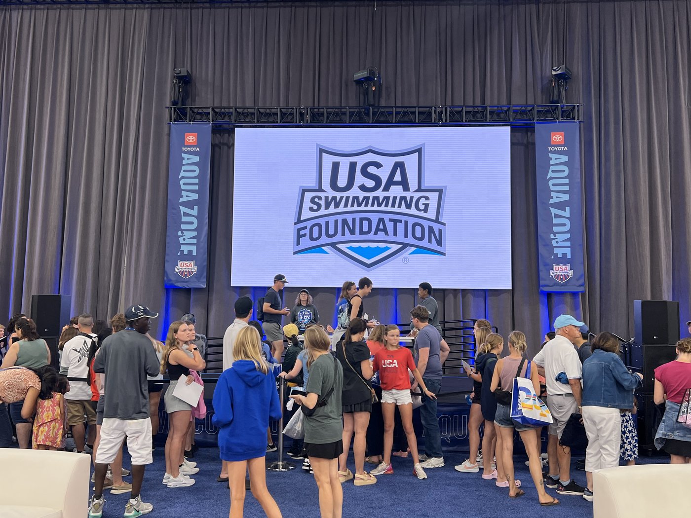 The Toyota Aqua Zone stage with a USA Swimming Foundation screen, Aqua Zone banners and a crowd of fans