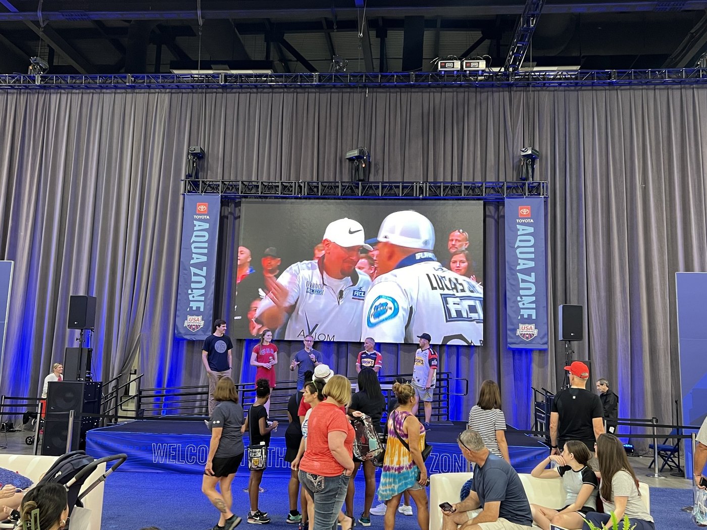 The Toyota Aqua Zone stage with a large screen showing a fishing broadcast, Aqua Zone banners and guests gathered in front
