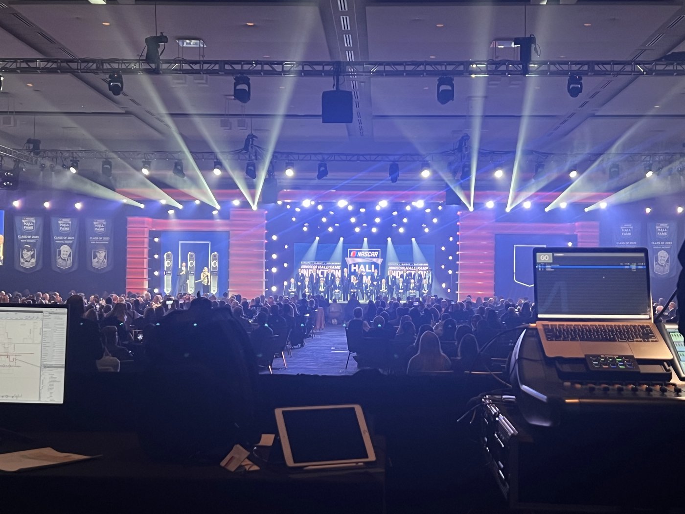The NASCAR Hall of Fame Induction stage seen from the show control desk, with beams of light across the ballroom