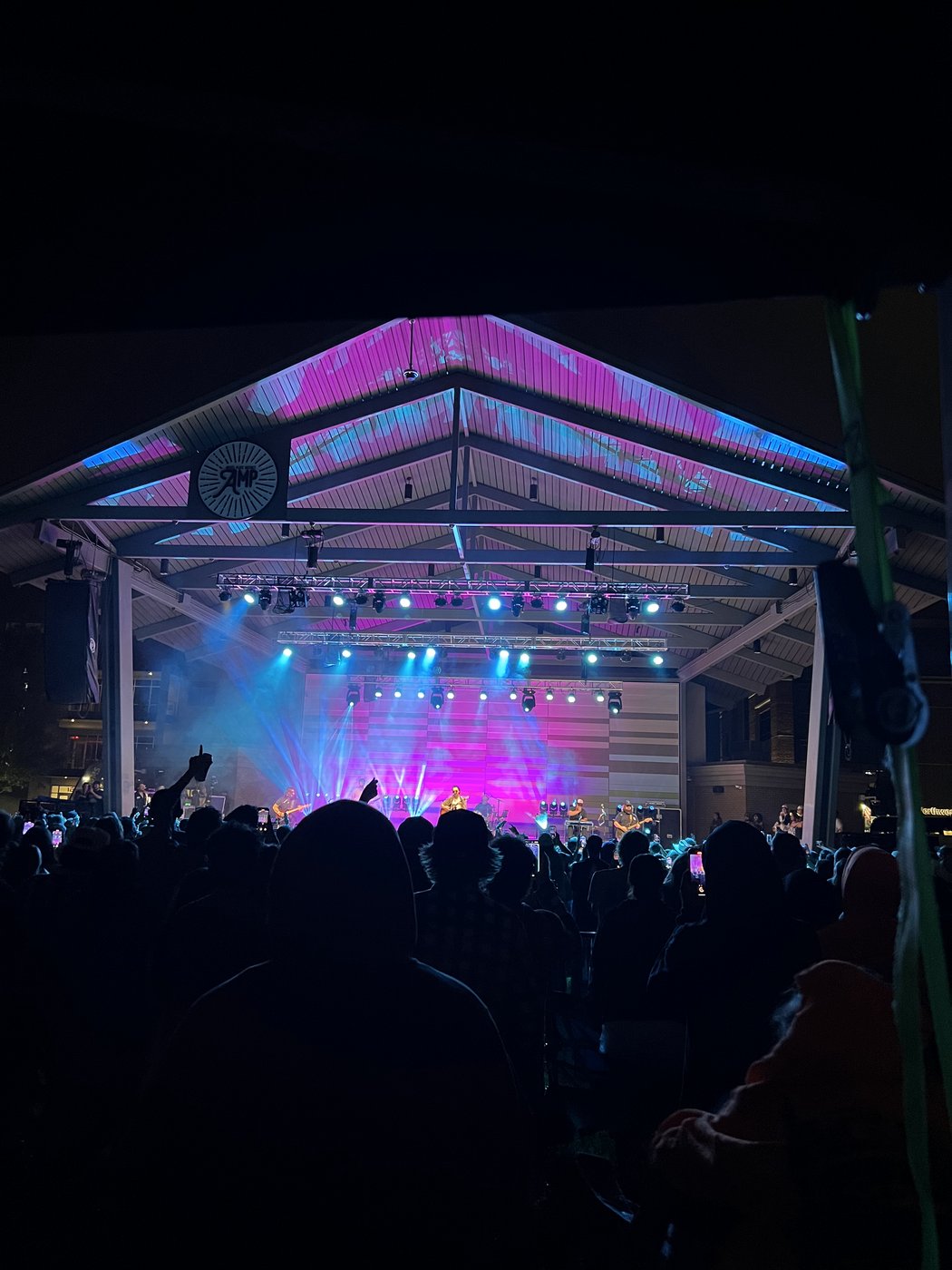An evening concert on the amphitheater stage with pink and blue lighting and a crowd in the foreground