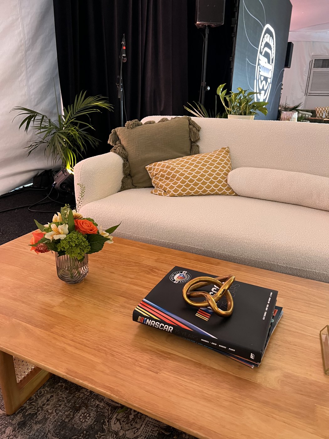Cream sofa, wood coffee table and florals inside the tent, with a NASCAR 75 Years book on the table