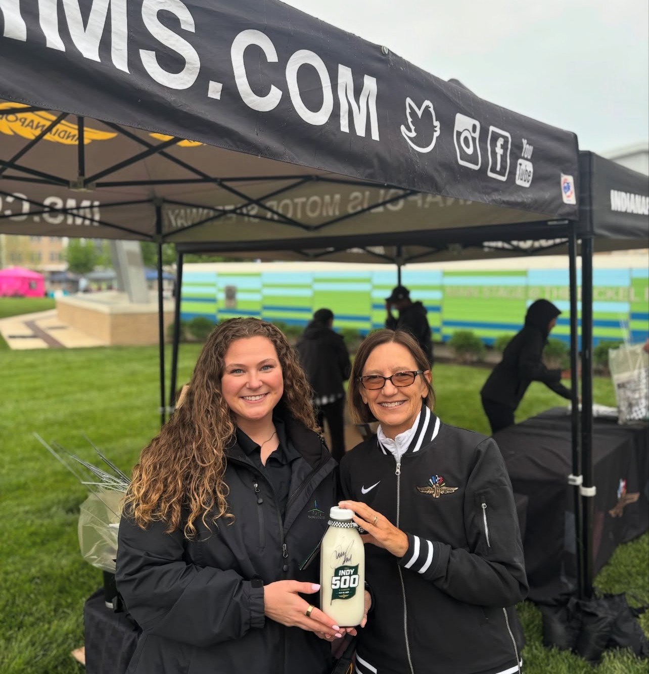 Alli Kaser and Allison Melangton of Penske Entertainment holding the 500 Festival Milk Jug under a tent